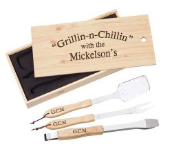 A wooden case with "Grillin-n-Chillin with the Mickelson's" engraved, containing three personalized grilling utensils: a spatula, a fork, and tongs, each marked with "G.C.M.